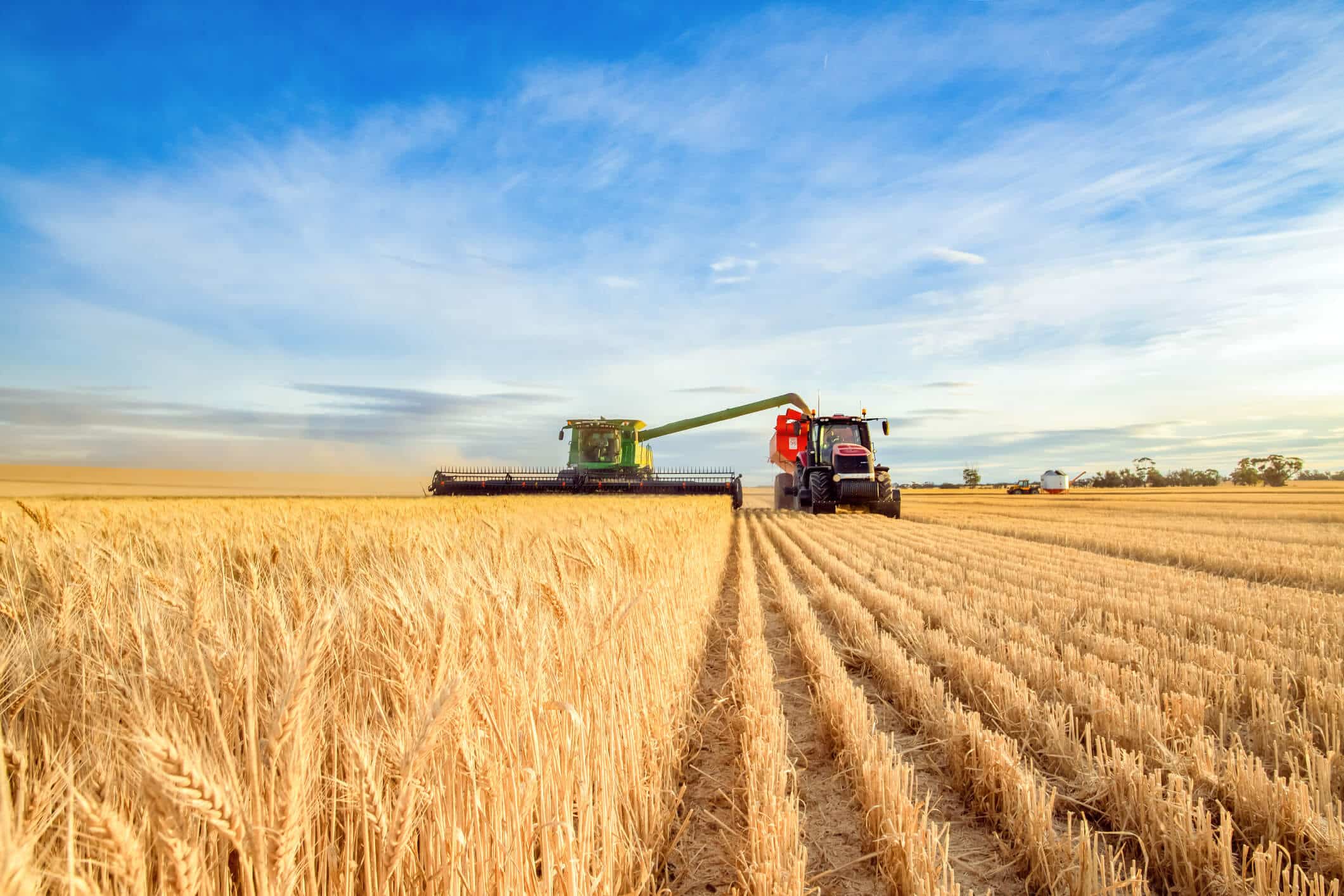 A tractor and combine harvester in a field on a sunny day representing Seamless final mile delivery for agricultural equipment