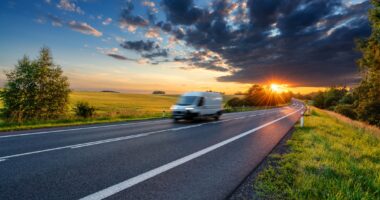 A Carousel Van Travelling Down The Road On A Delivery As The Sun Sets In The Background