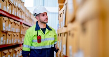 Side View Warehouse Worker Man Stand In Front Of The Shelves And Look To Product Box In Workplace.