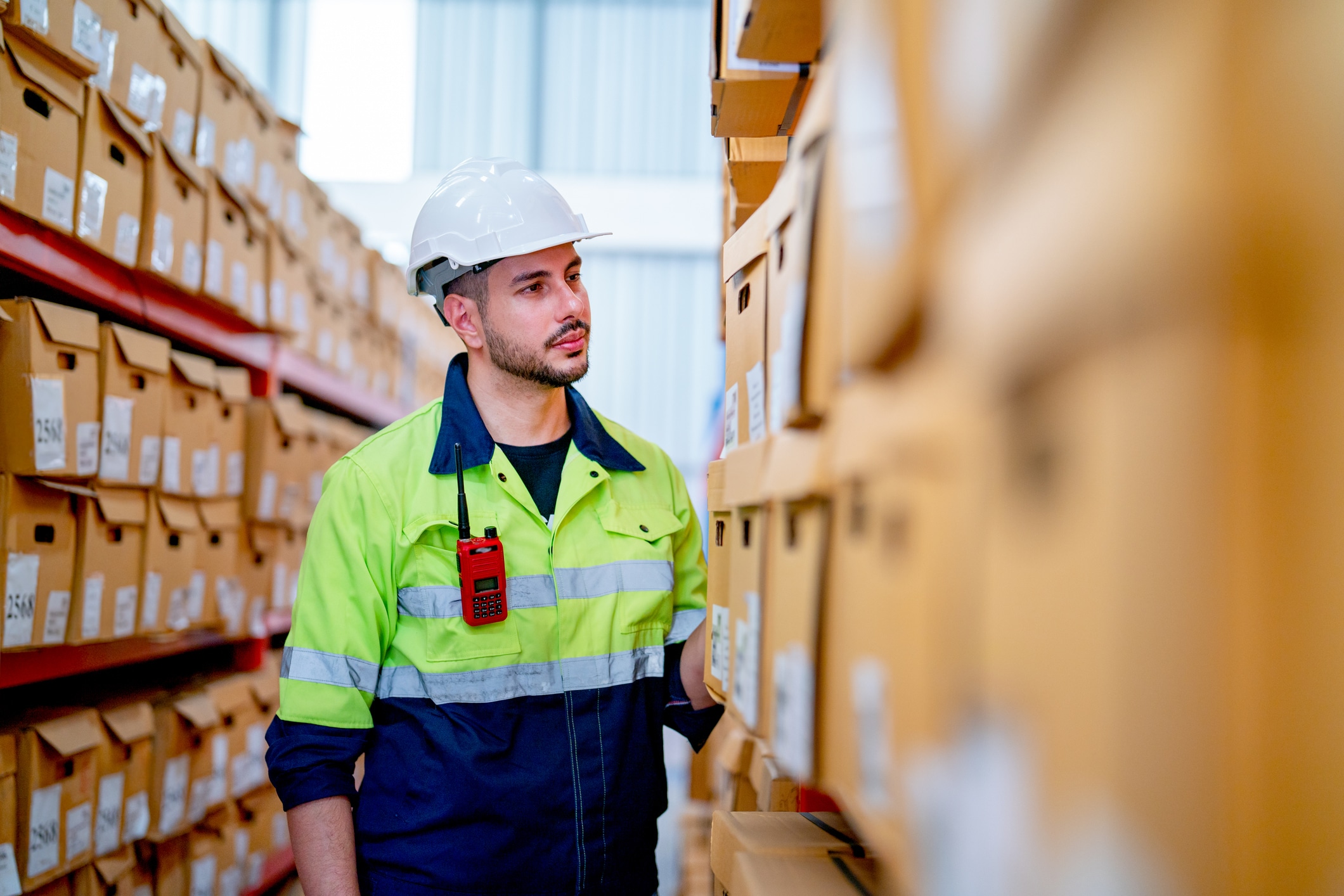 Side view warehouse worker man stand in front of the shelves and look to product box in workplace.