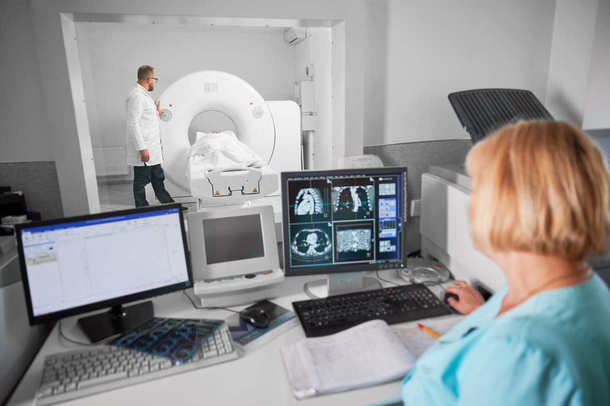 Blonde nurse sitting at computer, doctor standing, making MRI.